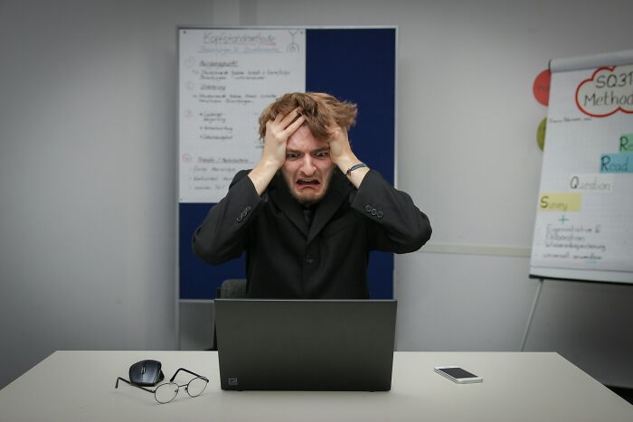Man frustrated at laptop, visibly upset by weaponized incompetence while working in an office setting.