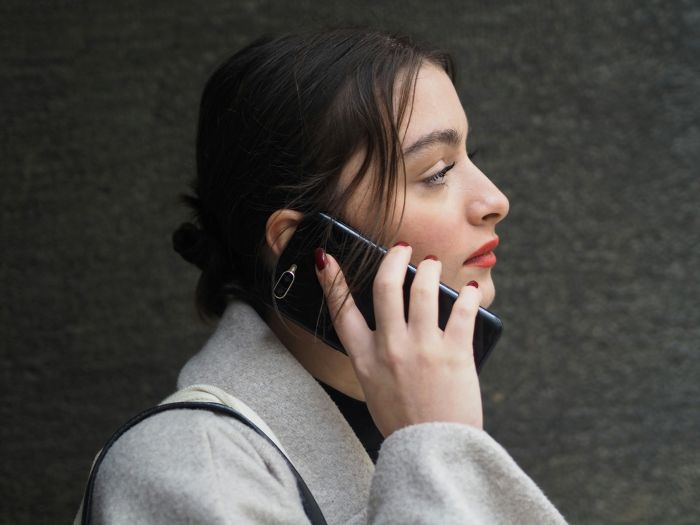 A woman in a grey coat on a phone call, potentially about a best friend skipping a wedding.