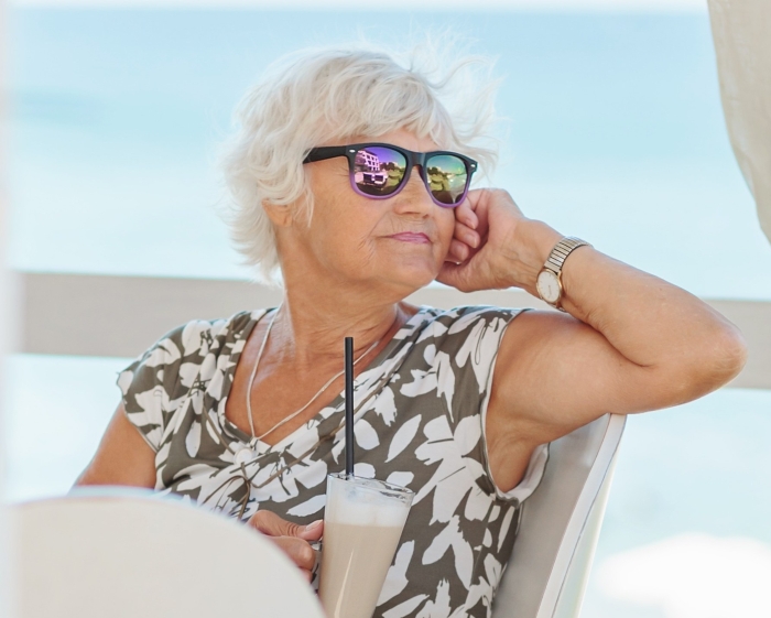A white-haired woman in sunglasses, holding a drink, looks thoughtful. This image could relate to the concept of entitlement.