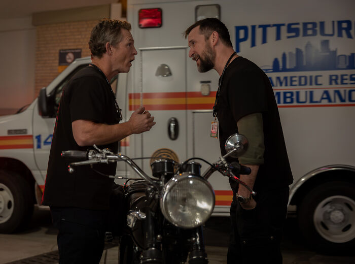 Dois homens de camisa preta conversando perto de uma motocicleta dentro de uma baia de ambulâncias em Pittsburgh, relacionado à atualização do criador do Pitt.