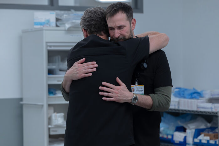 Dois homens se abraçam em um ambiente hospitalar, refletindo um momento emocionante relacionado ao criador de Pitt e à teoria do Dr.