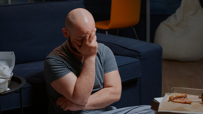 A distressed bald man sitting on the floor, holding his face in regret after a harsh lesson about chasing fantasy.