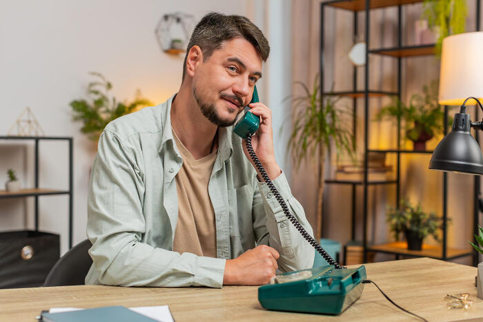 Man sitting at desk, speaking on a retro phone, surrounded by plants and modern office decor, illustrating infidelity stories.