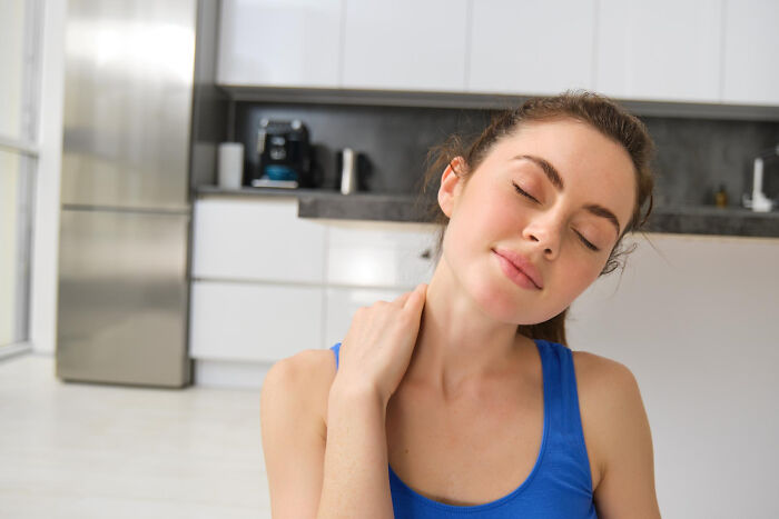 Young woman in a blue tank top sitting in a modern kitchen, appearing thoughtful amid stories of infidelity getting exposed.