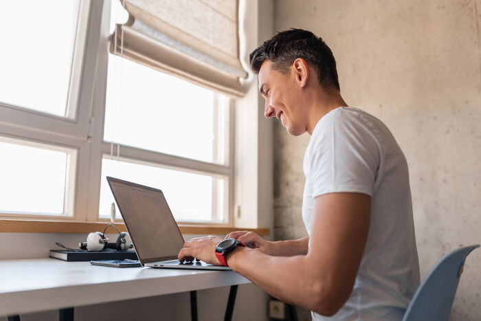 Man in white shirt typing on laptop near window, illustrating stories of infidelity getting exposed online.