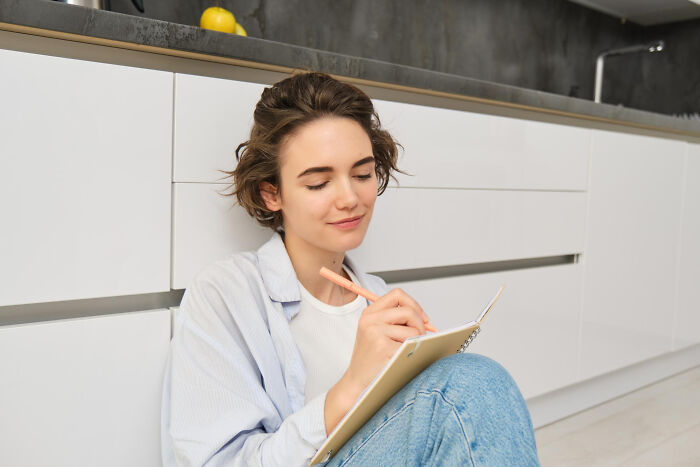Young woman sitting on the floor writing in a notebook, representing stories of infidelity and getting exposed.