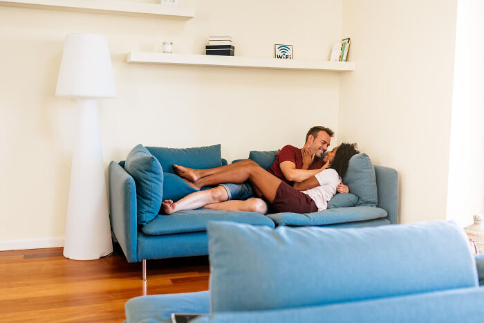 Couple embracing playfully on a blue couch, illustrating intimate moments related to infidelity stories getting exposed.