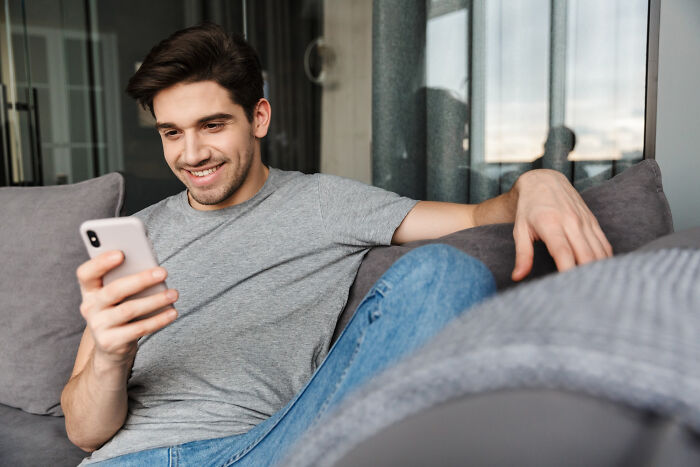 Young man smiling while reading a message on his phone, illustrating infidelity getting exposed stories.