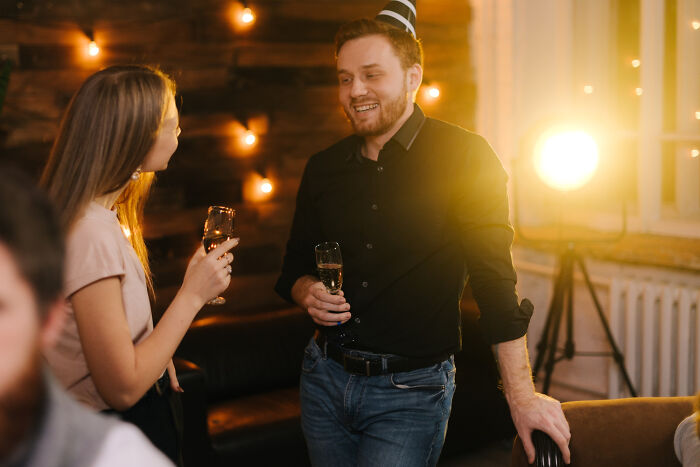 Man and woman chatting at a party holding drinks, illustrating wild stories of infidelity getting exposed in social settings.