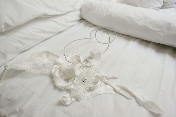 White lingerie and charger cable on a rumpled bed suggesting stories of infidelity getting exposed.