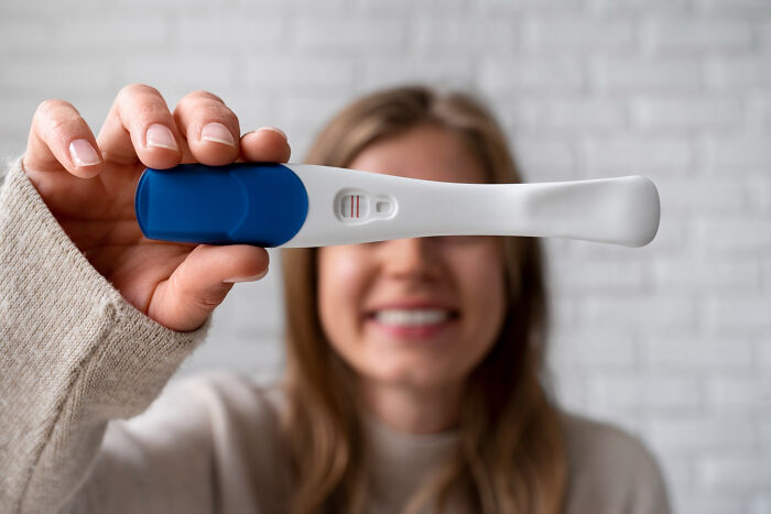 Woman smiling and holding a positive pregnancy test showing two lines, revealing unexpected news of infidelity exposed.
