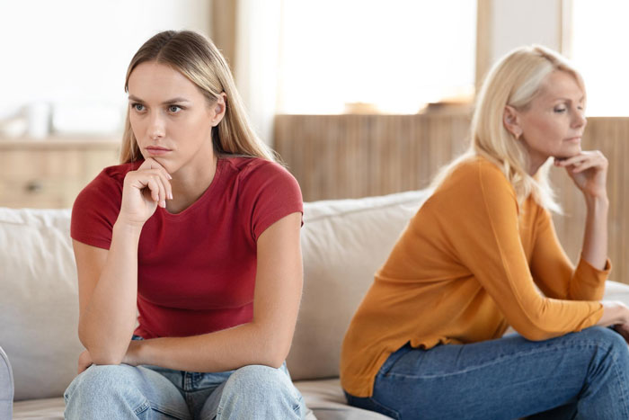 A young sister and her mom sitting separately on a couch, both looking upset. Mom's reaction to sister and brother.