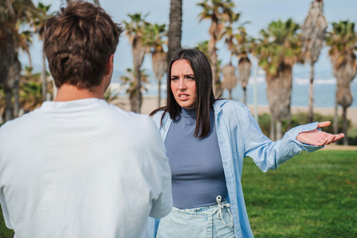Young woman discussing open affection in a polyamorous relationship with a partner at a park near palm trees.