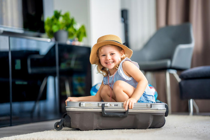 Smiling child in a hat sitting inside a suitcase, illustrating family dynamics in polyamorous relationships with open affection.