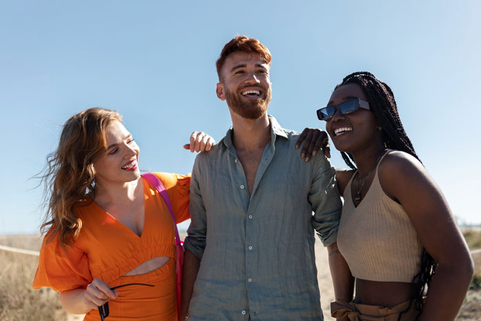 Three friends smiling outdoors, illustrating polyamorous relationship dynamics and open affection between partners.