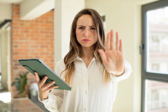 Woman in white shirt holding tablet with a stern expression, making a stop gesture as rude man snatches things without asking.