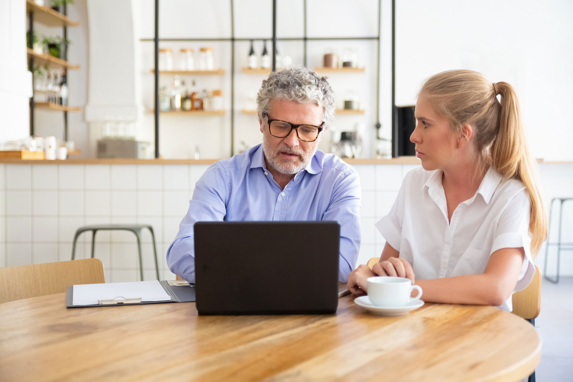 Man and woman having a serious discussion at table with laptop and coffee, illustrating rude coworker behavior and conflict.