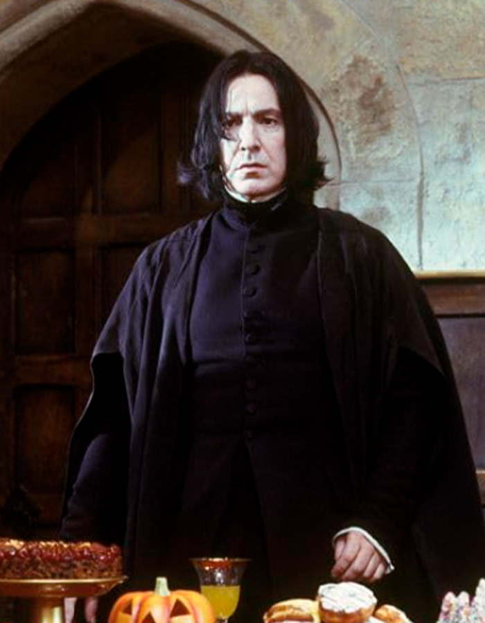 Actor dressed as Snape in a dark robe standing at a table with Halloween treats in a Harry Potter themed setting.