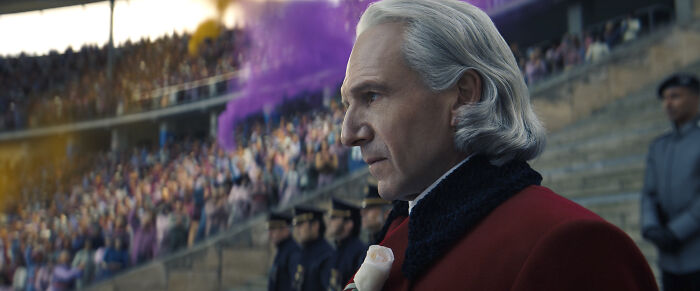 Character in The Hunger Games trailer stands in stadium with colorful smoke and crowd reacting to iconic moment.