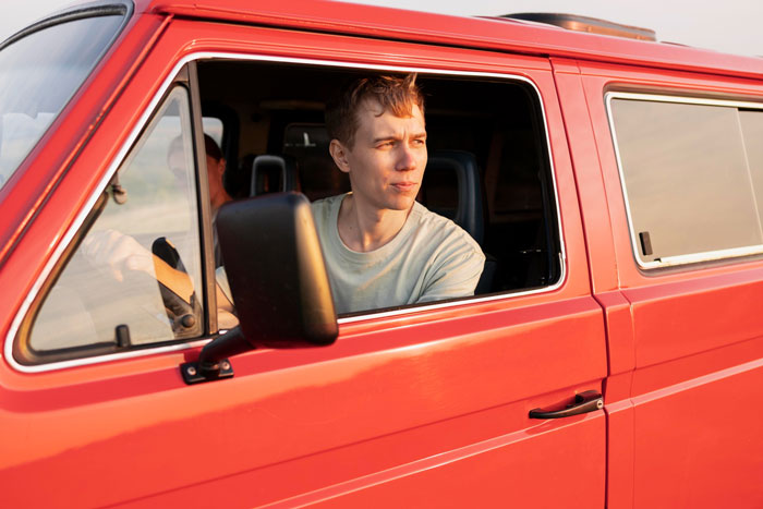 Young man sitting in a red van, representing a woman&rsquo;s parking spot conflict with entitled guests trapping the car.