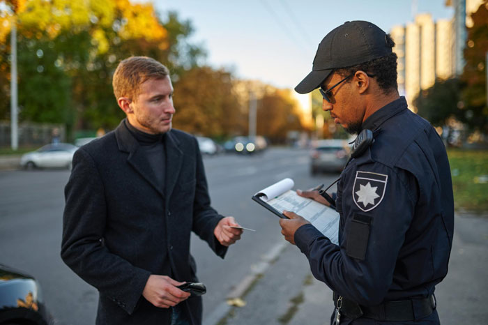 Police officer writing a ticket for a man after his car was trapped for taking a woman's parking spot by entitled guests.
