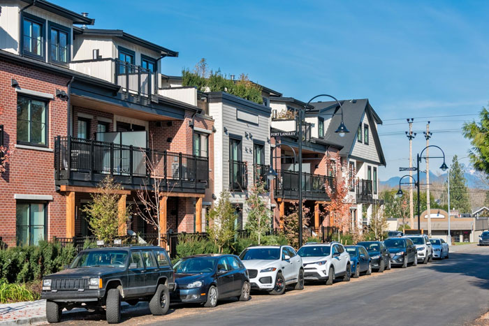 Residential street with multiple parked cars outside modern townhouses, illustrating woman&rsquo;s parking spot conflict with entitled guests.