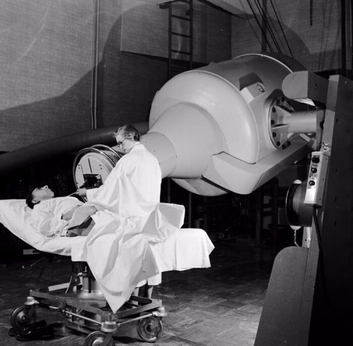 Vintage medical device in use showing early radiation therapy equipment with doctor attending patient on treatment table.