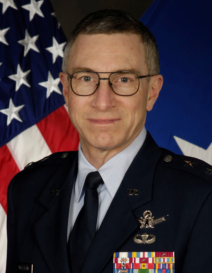 Senior military officer posing formally in uniform with US flag backdrop, representing concerns over missing or deceased scientists cases.