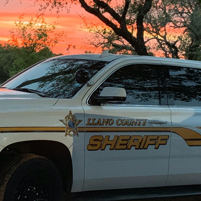 Um carro do xerife do condado de Llano sob um impressionante pôr do sol laranja. Esta cena destaca a presença de agentes da lei, pertinente à acusação de professor substituto.