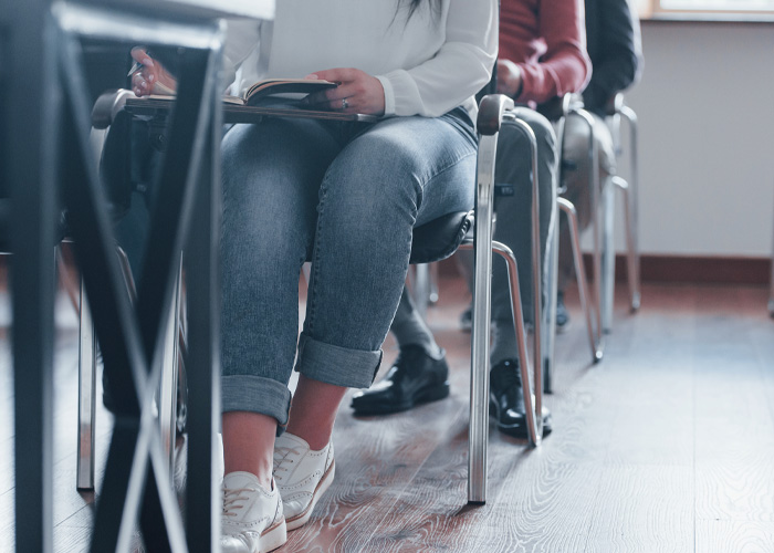 Uma fila de alunos em uma sala de aula, com a pessoa mais próxima vestindo jeans, segurando um livro, destacando a necessidade de uma boa conduta do professor substituto.