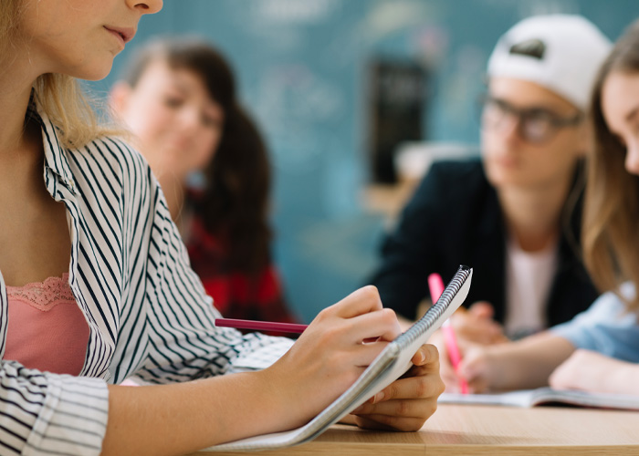 Um aluno escrevendo anotações com um lápis em uma sala de aula, evocando temas em torno do 