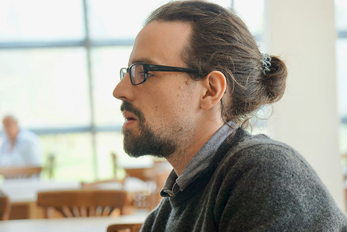 Young man with glasses and a bun, wearing a gray sweater, showing a subtle and interesting display of intelligence.