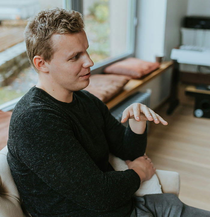 Man in a black sweater gesturing thoughtfully indoors, illustrating subtle and interesting displays of intelligence.