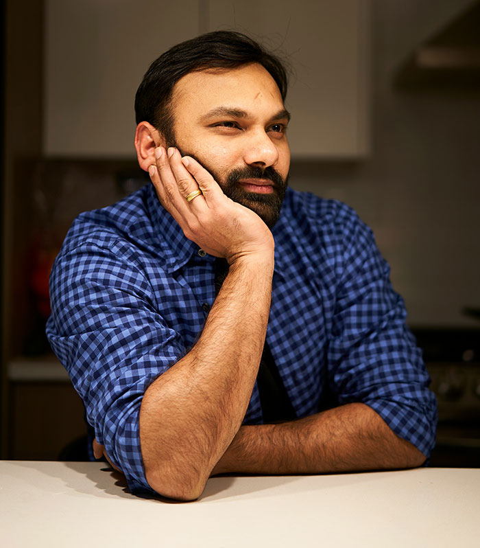 Man in a blue checkered shirt resting his face on his hand, displaying a subtle and interesting display of intelligence.