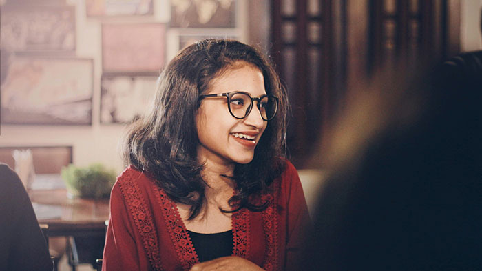 Young woman wearing glasses and a red top, smiling and engaging in a subtle and interesting display of intelligence.