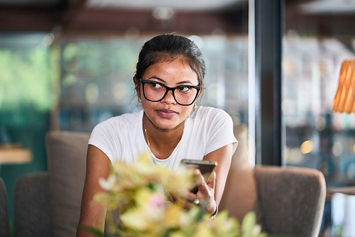Young woman wearing glasses, holding a smartphone and showing subtle displays of intelligence in a casual setting
