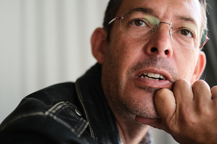 Close-up of a man wearing glasses and a leather jacket, thoughtfully displaying subtle and interesting intelligence.