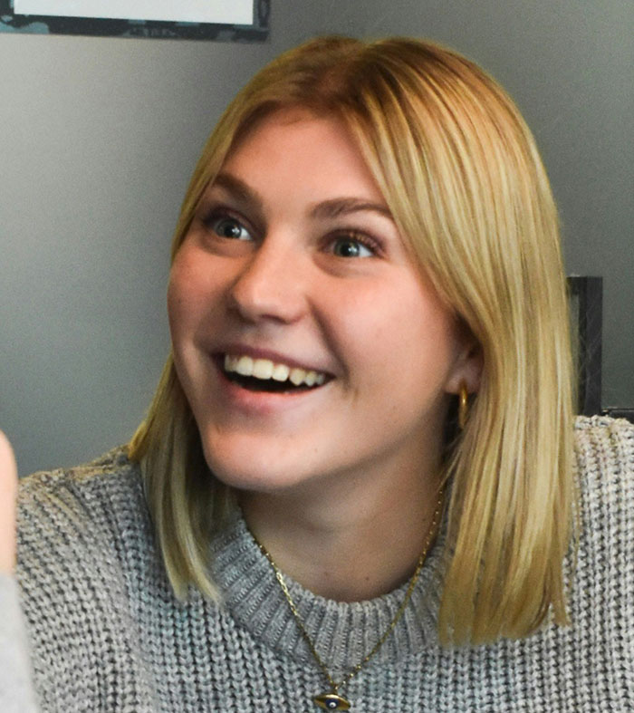 Young woman with blonde hair smiling, showing subtle and interesting displays of intelligence in a casual setting.