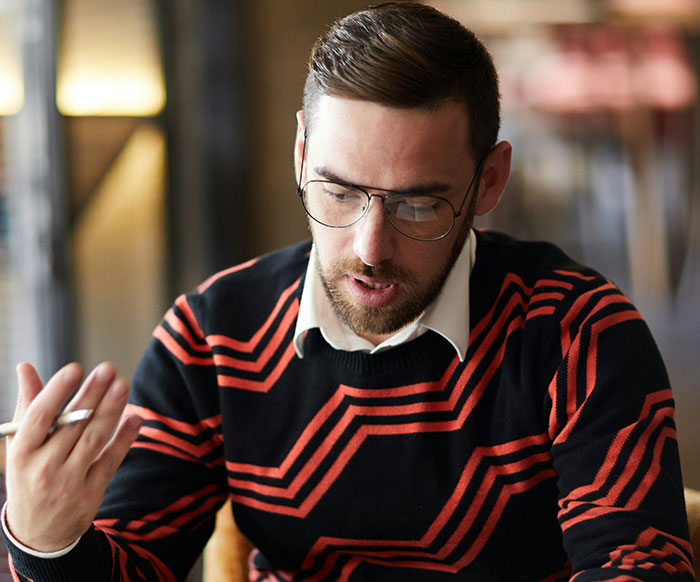 Man wearing glasses and a patterned sweater showing subtle displays of intelligence during a focused conversation indoors.