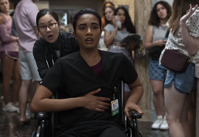 A distressed doctor in a wheelchair clutching her chest as a nurse and onlookers react to a major cast shake up in The Pitt.