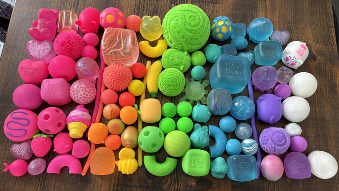 Colorful bulk items sorted by shades of pink, orange, green, blue, and purple in an organized display on wood surface. Colorful bulk items sorted by shades of pink, orange, green, blue, and purple in an organized display on wood surface.