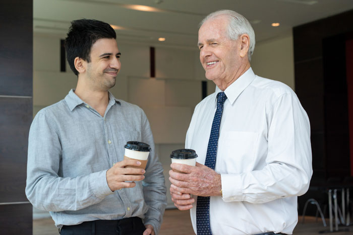 Two men holding coffee cups, smiling and having a friendly conversation in a modern office setting. Two men holding coffee cups, smiling and having a friendly conversation in a modern office setting.
