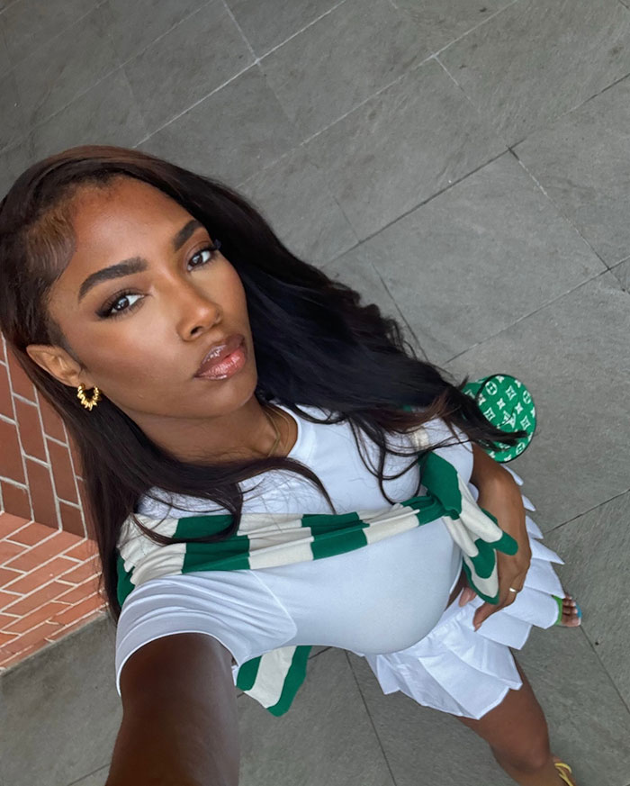 Glamorous influencer taking a selfie outdoors wearing white and green, fans notice something off in the post.