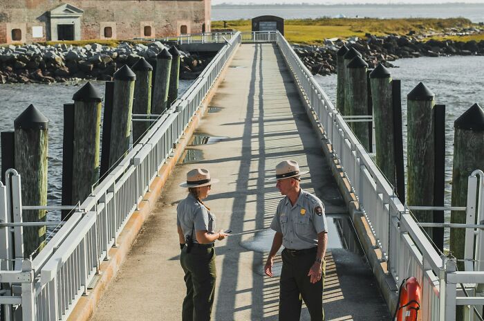 Two park rangers in uniform talking on a sunny pier, illustrating random life decisions leading people to the right place.
