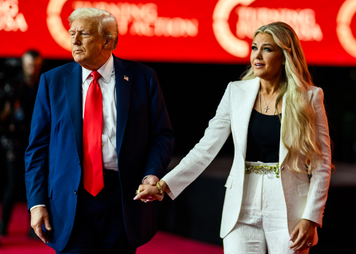 Homem de terno azul e gravata vermelha de mãos dadas com uma mulher de terno branco, destacando a revolta dos adolescentes por causa da polêmica visita ao colégio.