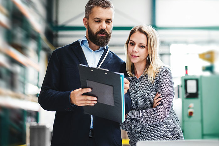 Manager reviewing clipboard with female worker in industrial setting, illustrating management chews out worker SEO concept.