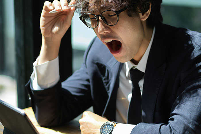 Stressed worker in glasses yawning while wearing business attire, illustrating management chews out worker scenario.