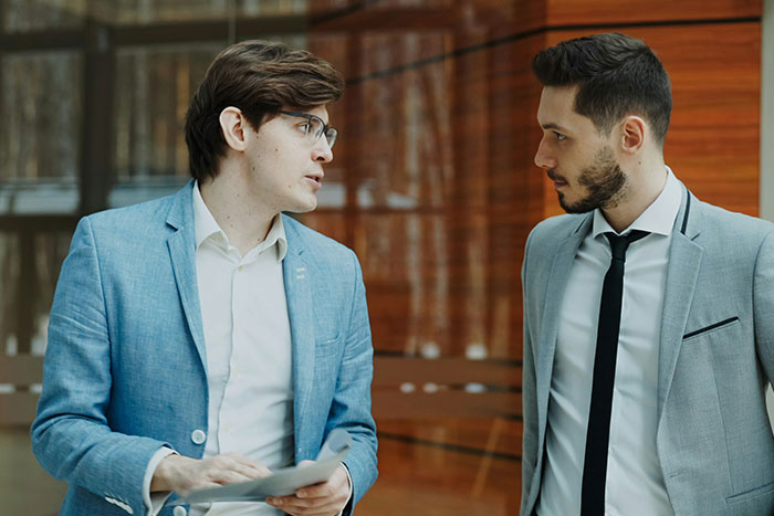 Two business professionals in suits having a serious discussion about management and worker performance in an office setting