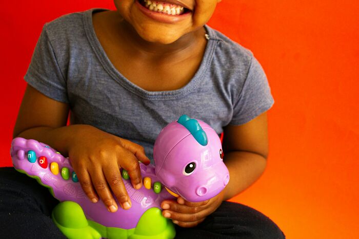 Child holding a colorful educational toy dinosaur, smiling against a bright orange background, sharing parenting tips.