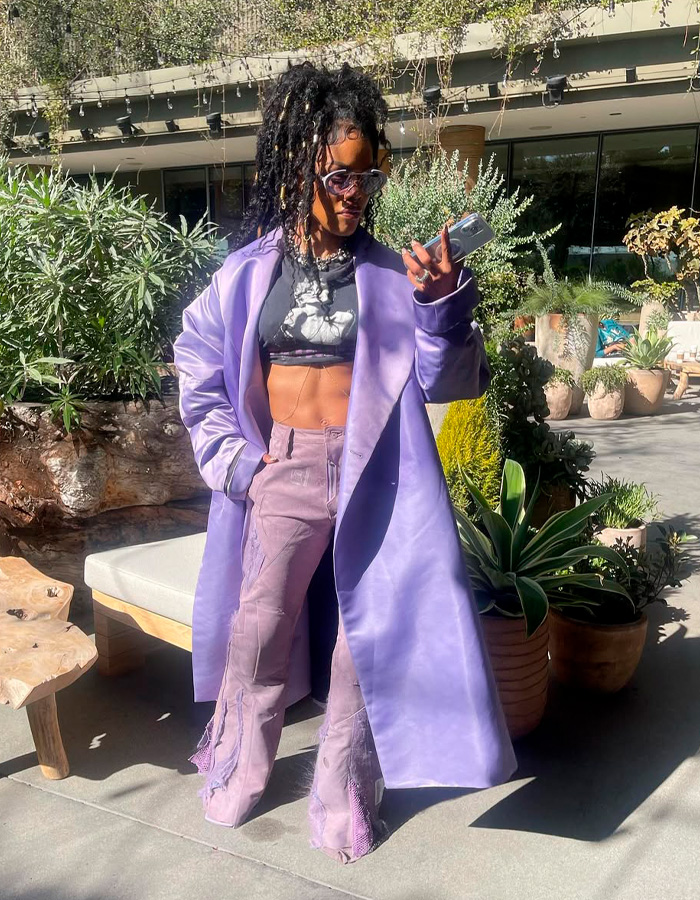 Teyana Taylor showing toned abs in lilac coat and stylish pants outdoors, fans excited by her Coachella look.